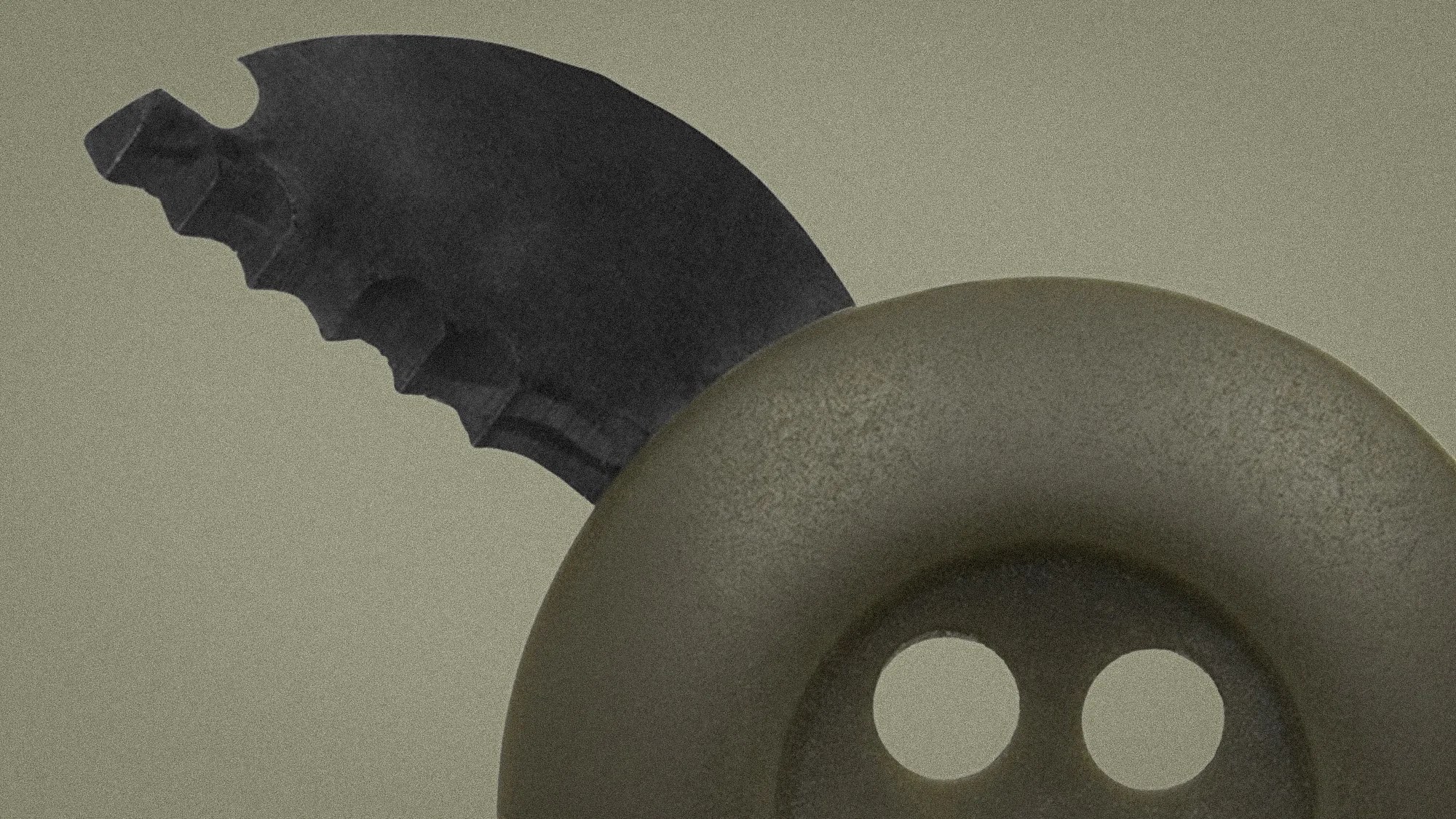 Close-up of a black serrated knife blade partially inserted into a large, dark gray button with two holes.