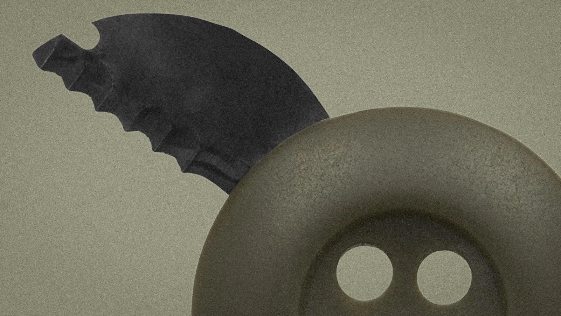 Close-up of a black serrated knife blade partially inserted into a large, dark gray button with two holes.