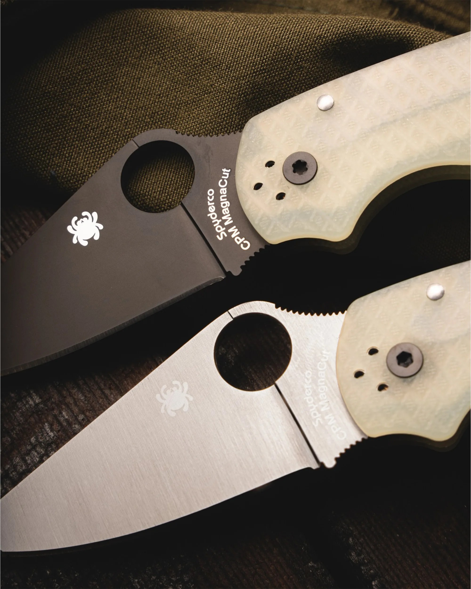 Two Spyderco folding knives with translucent textured handles, one with a black blade and the other with a silver blade, on dark fabric.
