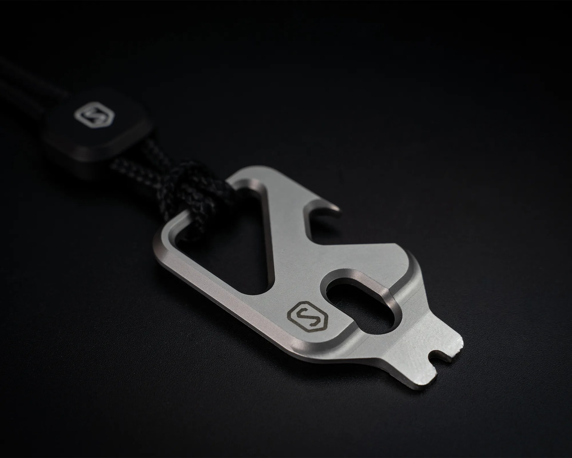 Silver multi-tool keychain with a black cord and engraved logo on a black surface.