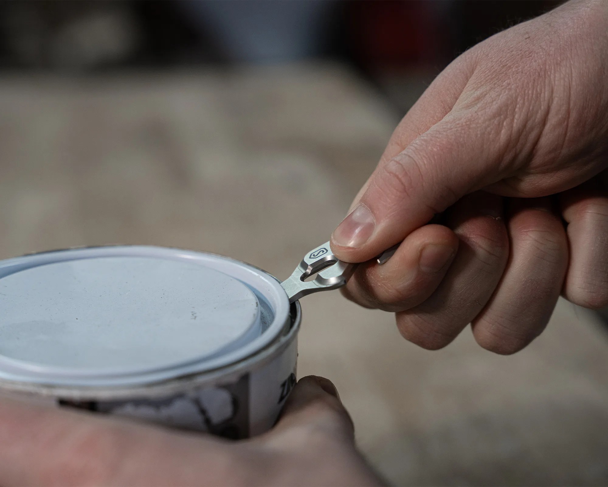 Hand using a small metal tool to pry open the lid of a paint can.