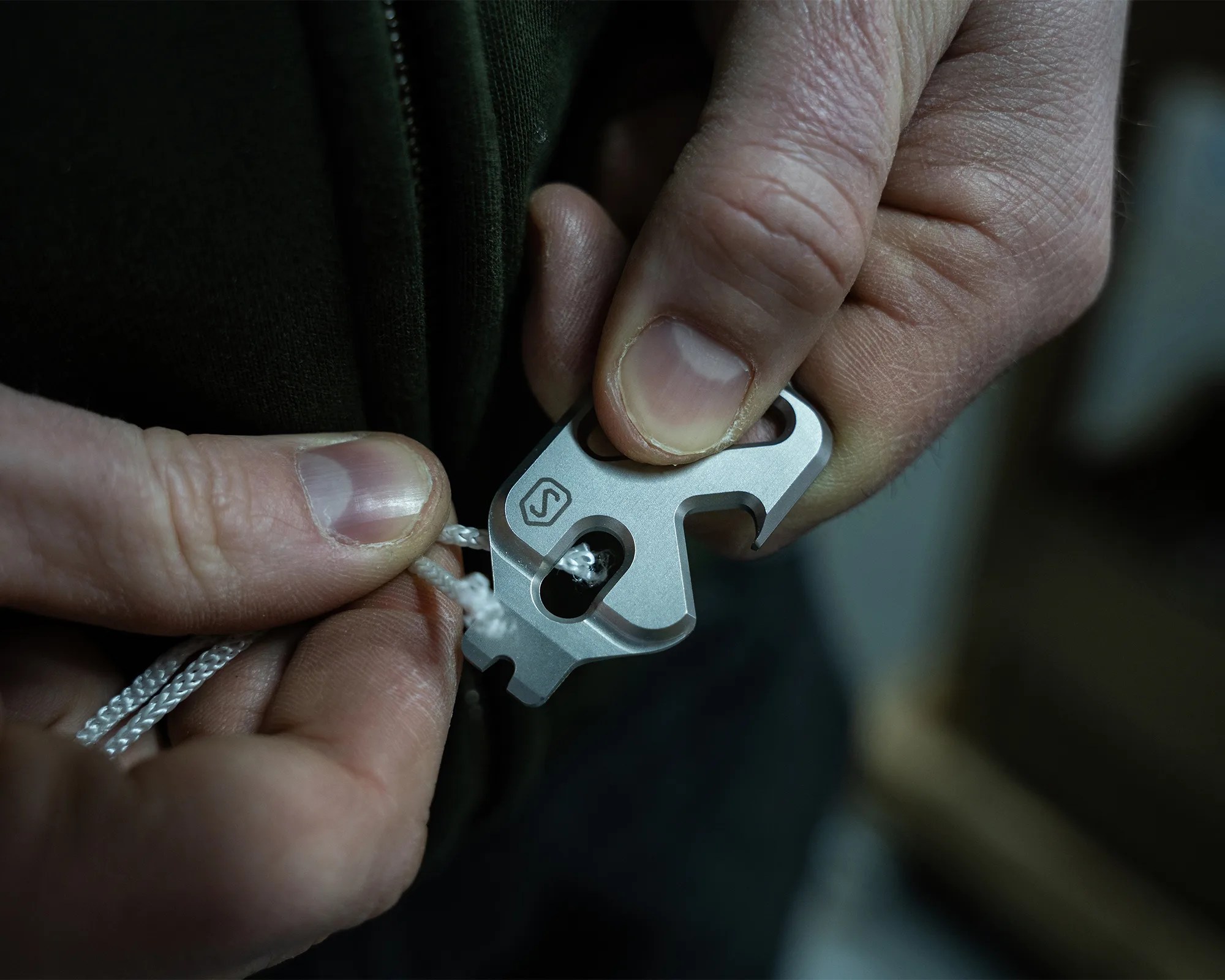 Close-up of hands threading a white cord through a silver multi-tool with a logo on it.