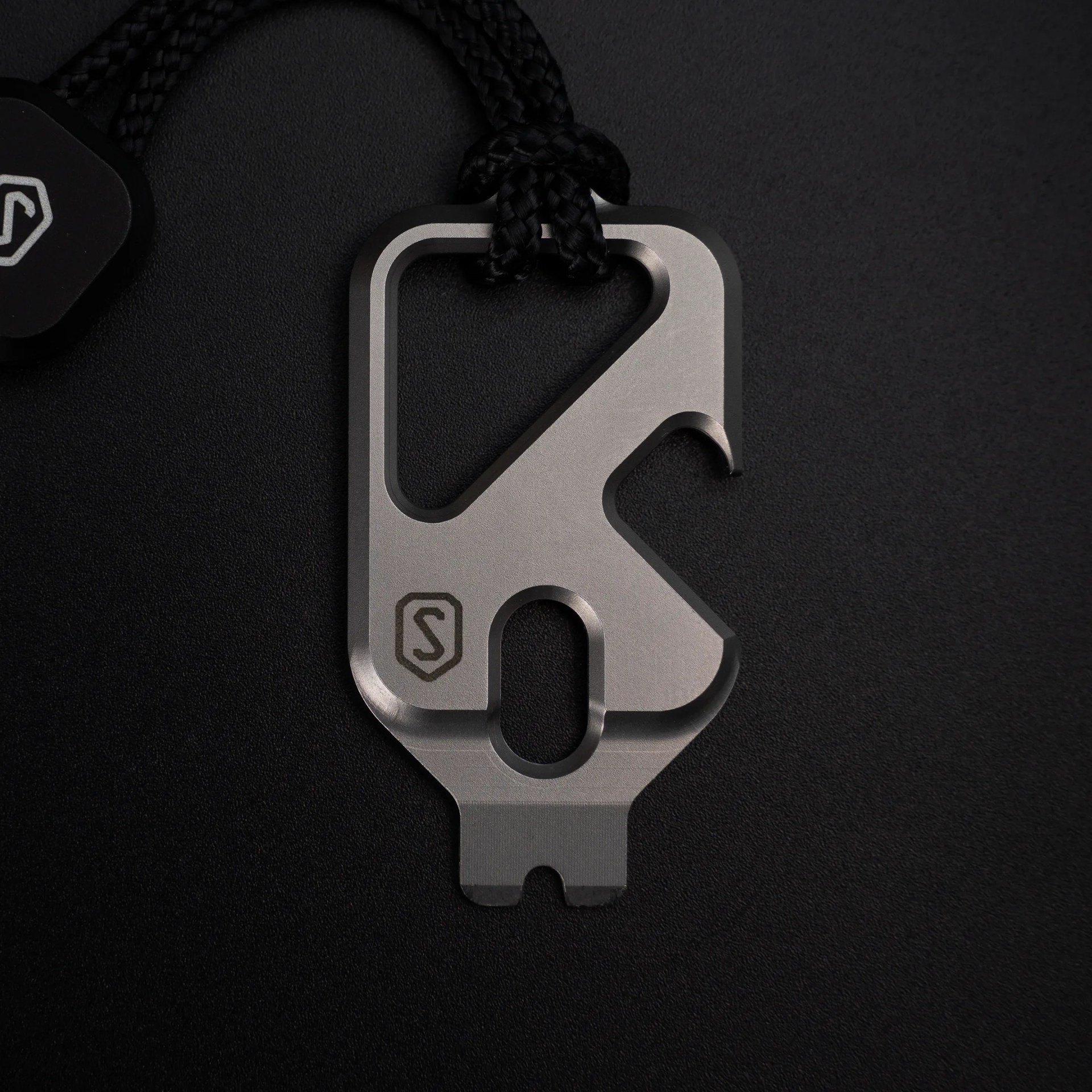 Matte silver multi-tool with a black cord attached, featuring various cutouts and a small logo.