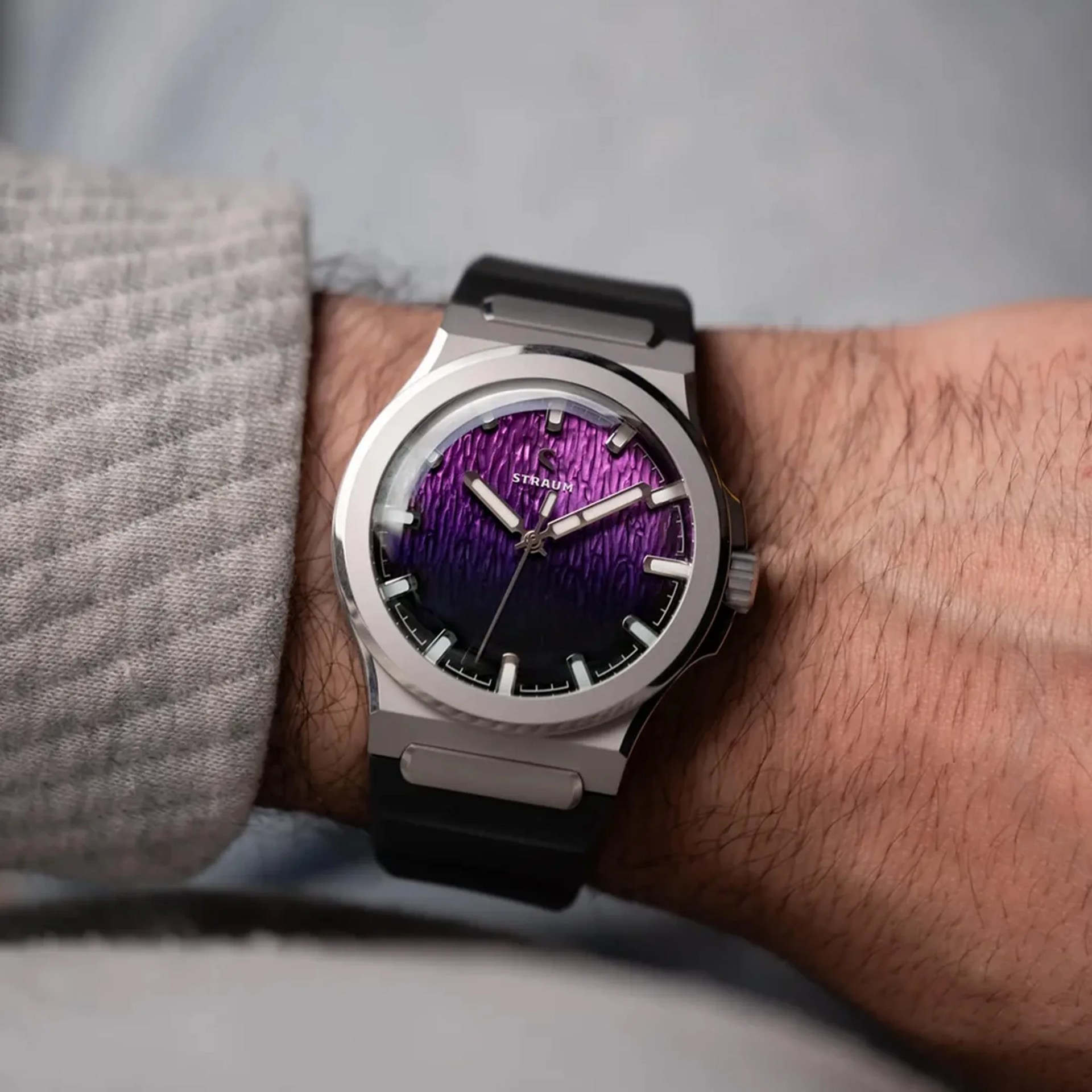 Silver wristwatch with textured purple and black gradient dial and black strap worn on a wrist.