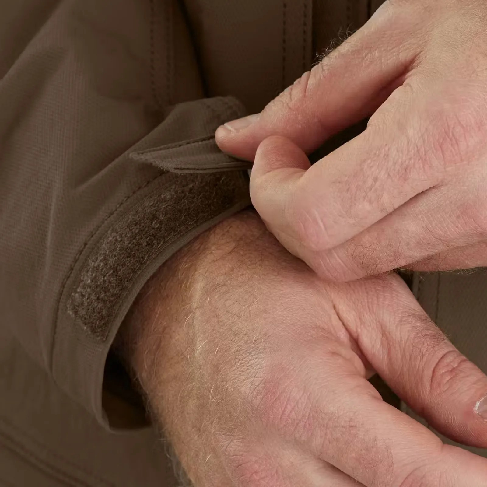 Close-up of a hand adjusting the brown fabric cuff with Velcro on a jacket sleeve.