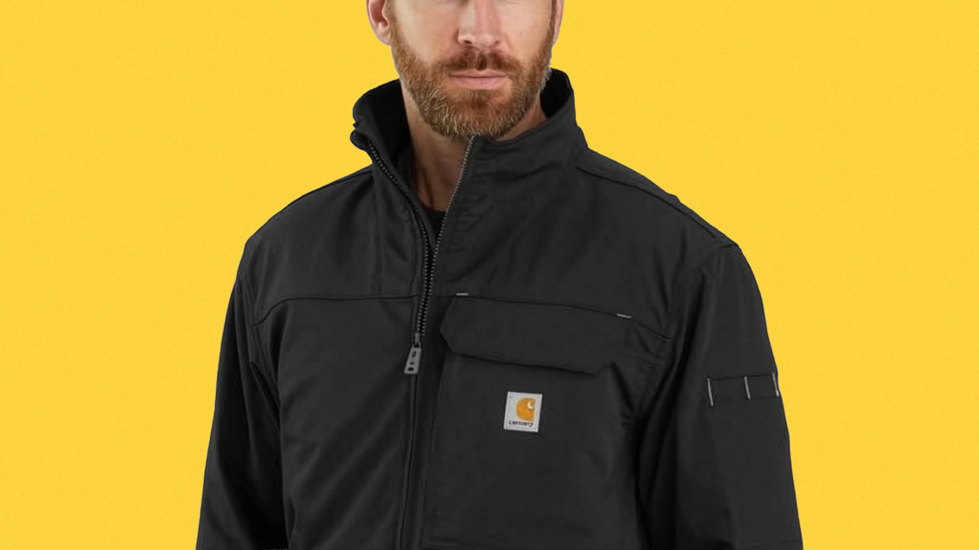 Black Carhartt zip-up jacket with chest pocket and logo patch on a person against a yellow background.