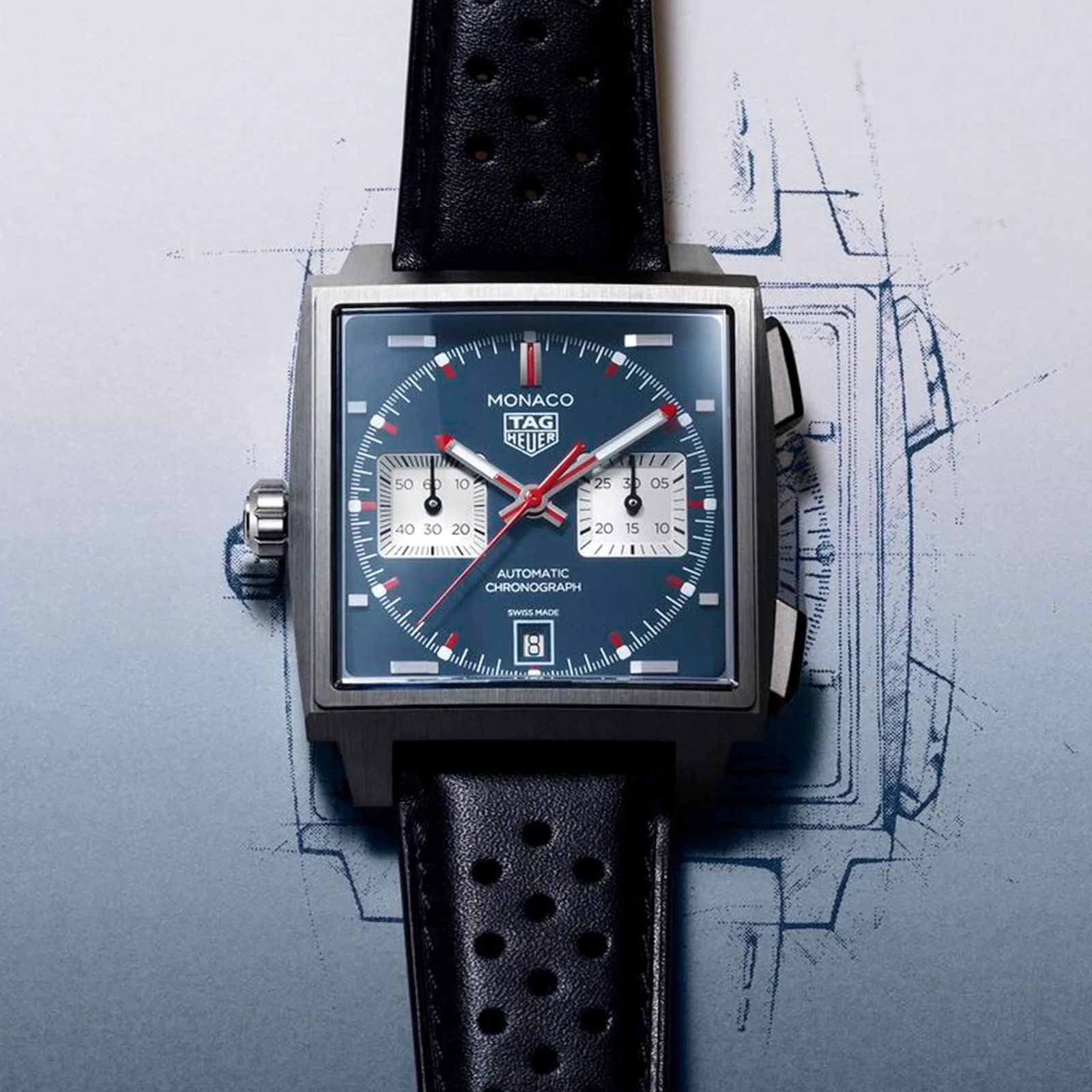 Square TAG Heuer Monaco watch with blue dial, two white subdials, red accents, and perforated black leather strap.