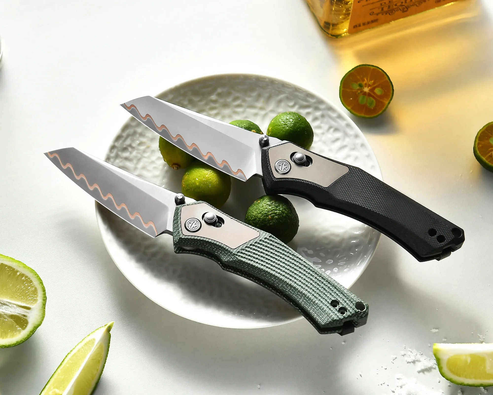 Two folding knives with textured handles, one black and one green, with wavy-edged blades on a white plate with green limes.