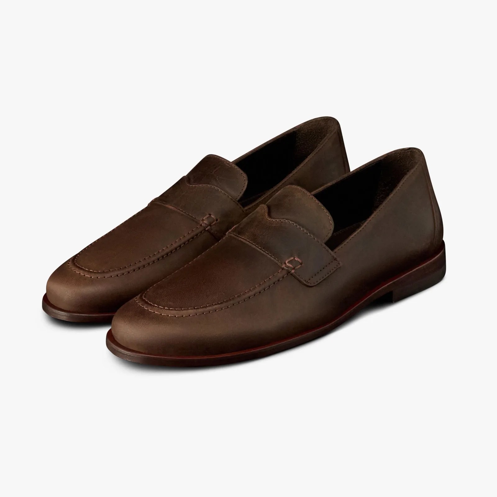 Pair of brown leather slip-on loafers with stitched detailing and low heels on a white background.