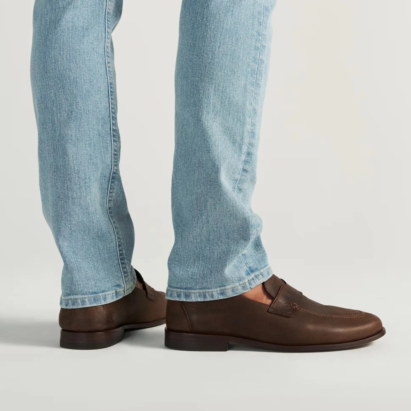 Brown leather loafers worn with light blue denim jeans.