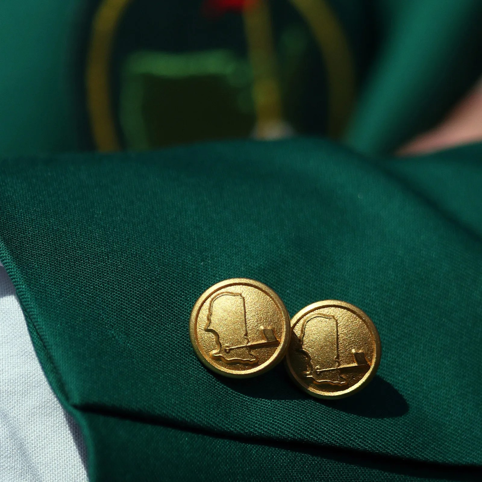 Pair of gold-colored round cufflinks with a raised profile design on a dark green fabric.