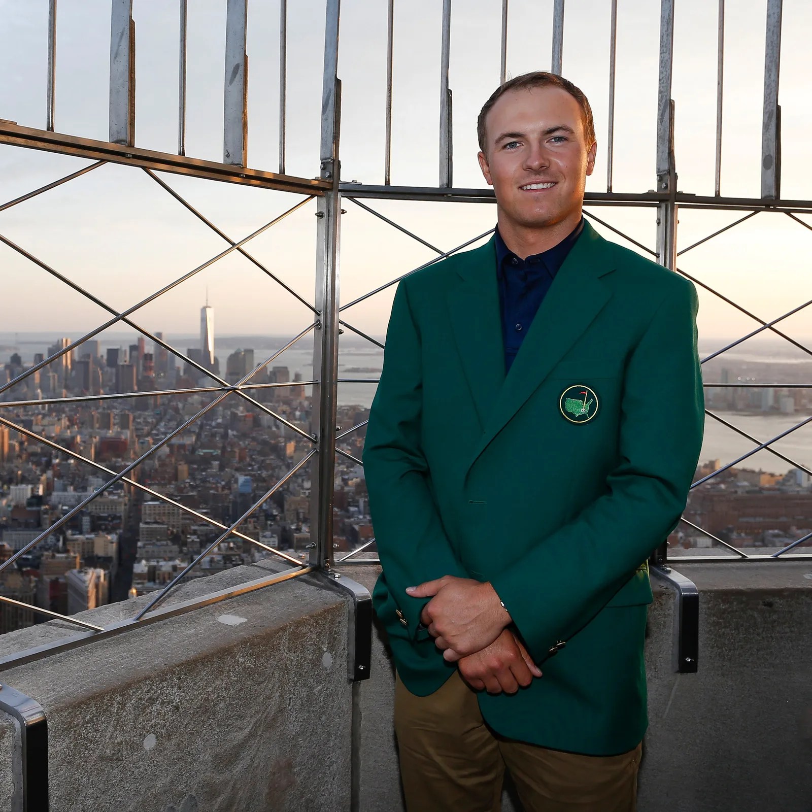 Man wearing a green Masters golf jacket standing on a rooftop with a city skyline in the background.