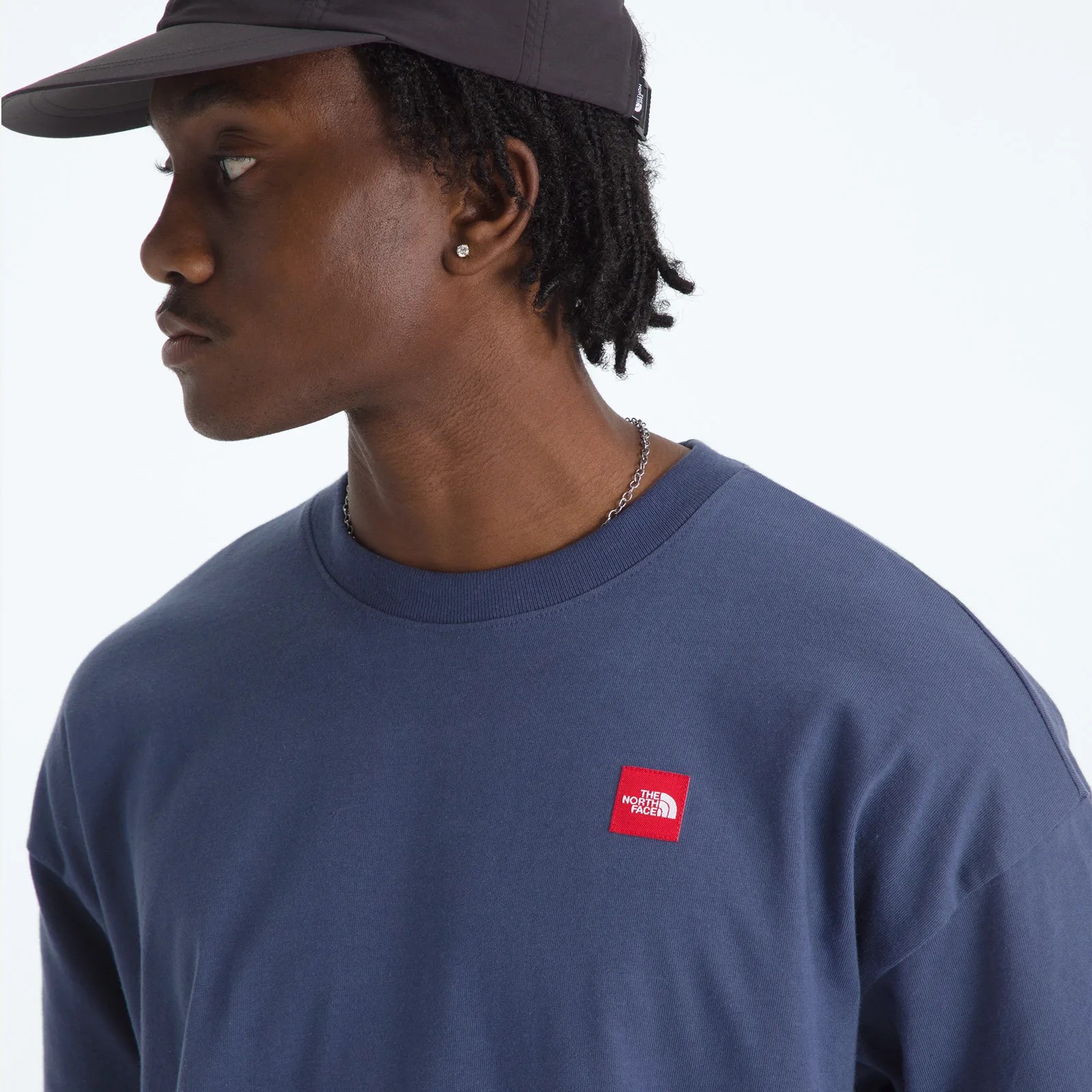 Man wearing a navy blue sweatshirt with a red The North Face logo patch on the chest and a black cap.
