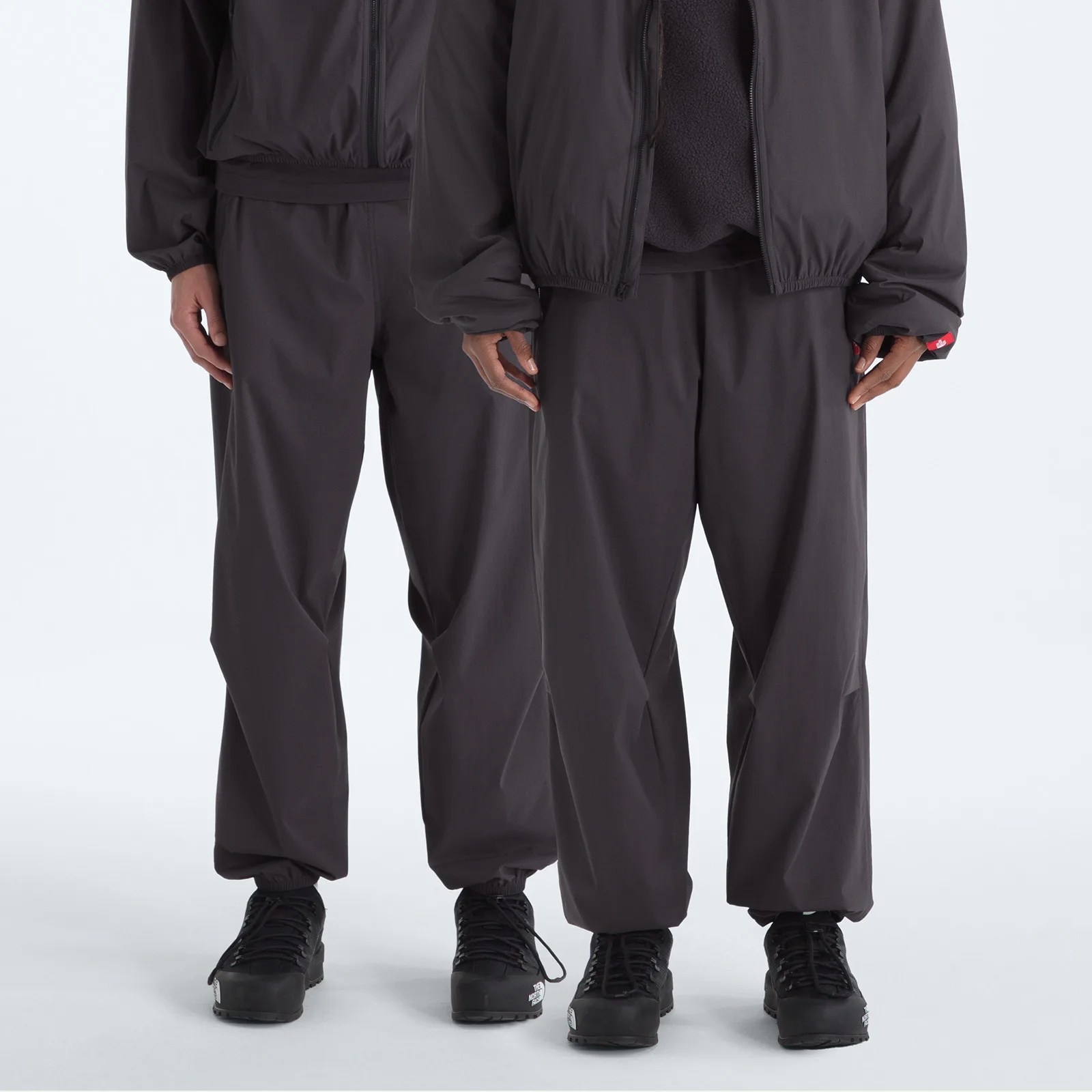 Two people wearing matching black loose-fit pants and black hiking boots standing side by side.