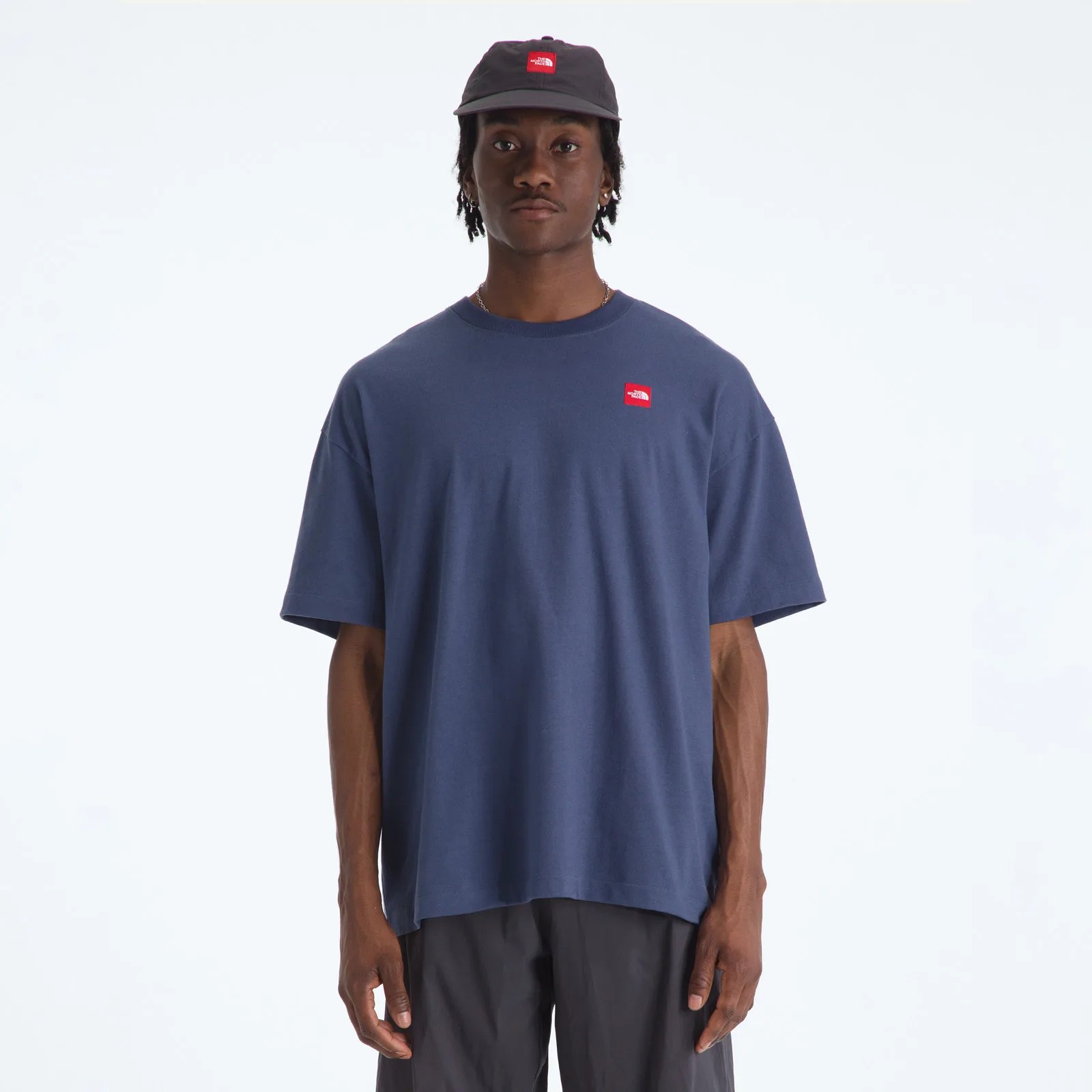 Navy blue oversized T-shirt with a small red logo on the chest worn by a person.