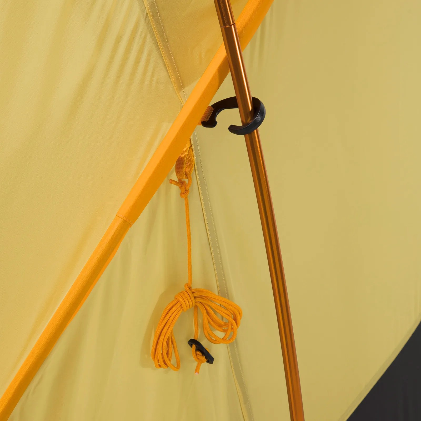 Close-up of yellow tent fabric with orange pole, black clip, and coiled orange guy line attached.