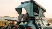 Green rooftop tent with sleeping bags mounted on a teal SUV with two mountain bikes on the rear rack.