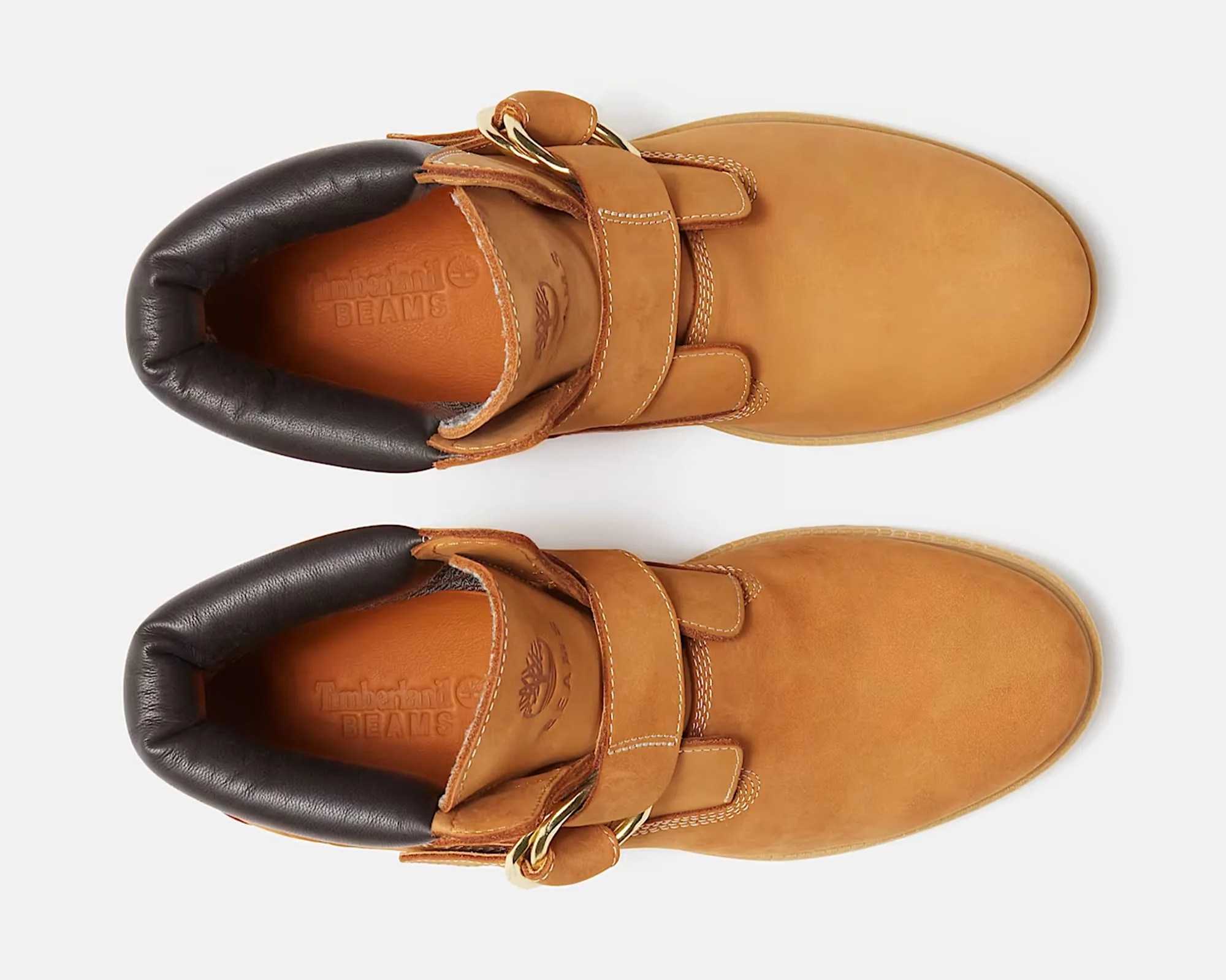 Pair of tan leather Timberland boots with black padded collars and gold buckle straps, viewed from above.