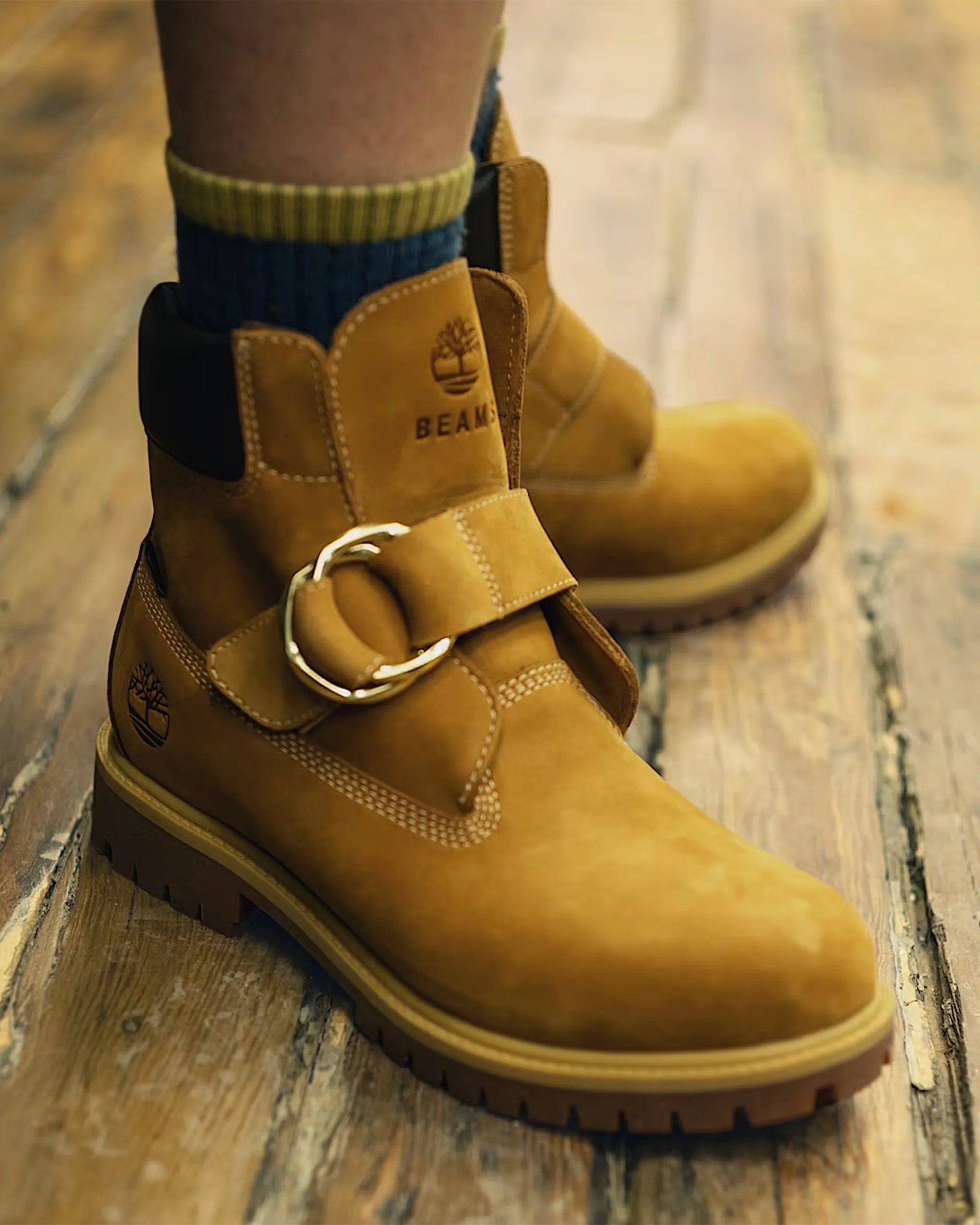 Tan leather boots with a gold buckle and black padded collar worn on wooden floor.