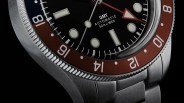 Close-up of a stainless steel GMT automatic watch with a black dial and red and blue bezel showing 50m water resistance.
