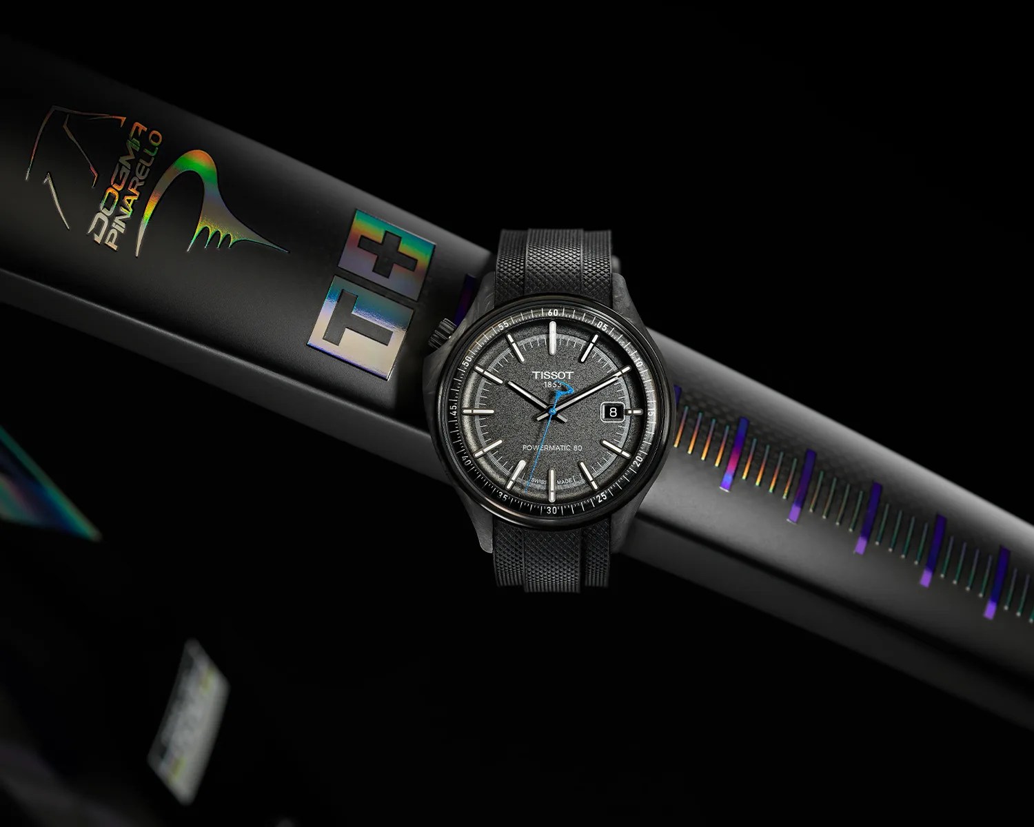 Black Tissot Powermatic 80 wristwatch with textured dial and blue second hand on a black Dom Pinarello bicycle frame.