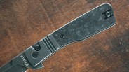 Close-up of a black folding knife handle with textured grip and "FINCH" logo on a wooden surface.