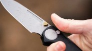 Close-up of a hand holding a black folding knife with water droplets on the silver blade.