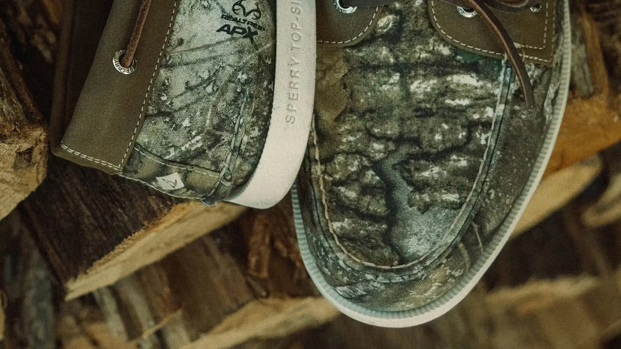 Close-up of camo-patterned Sperry Top-Sider boat shoes with brown leather accents on stacked firewood.