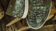 Close-up of camo-patterned Sperry Top-Sider boat shoes with brown leather accents on stacked firewood.