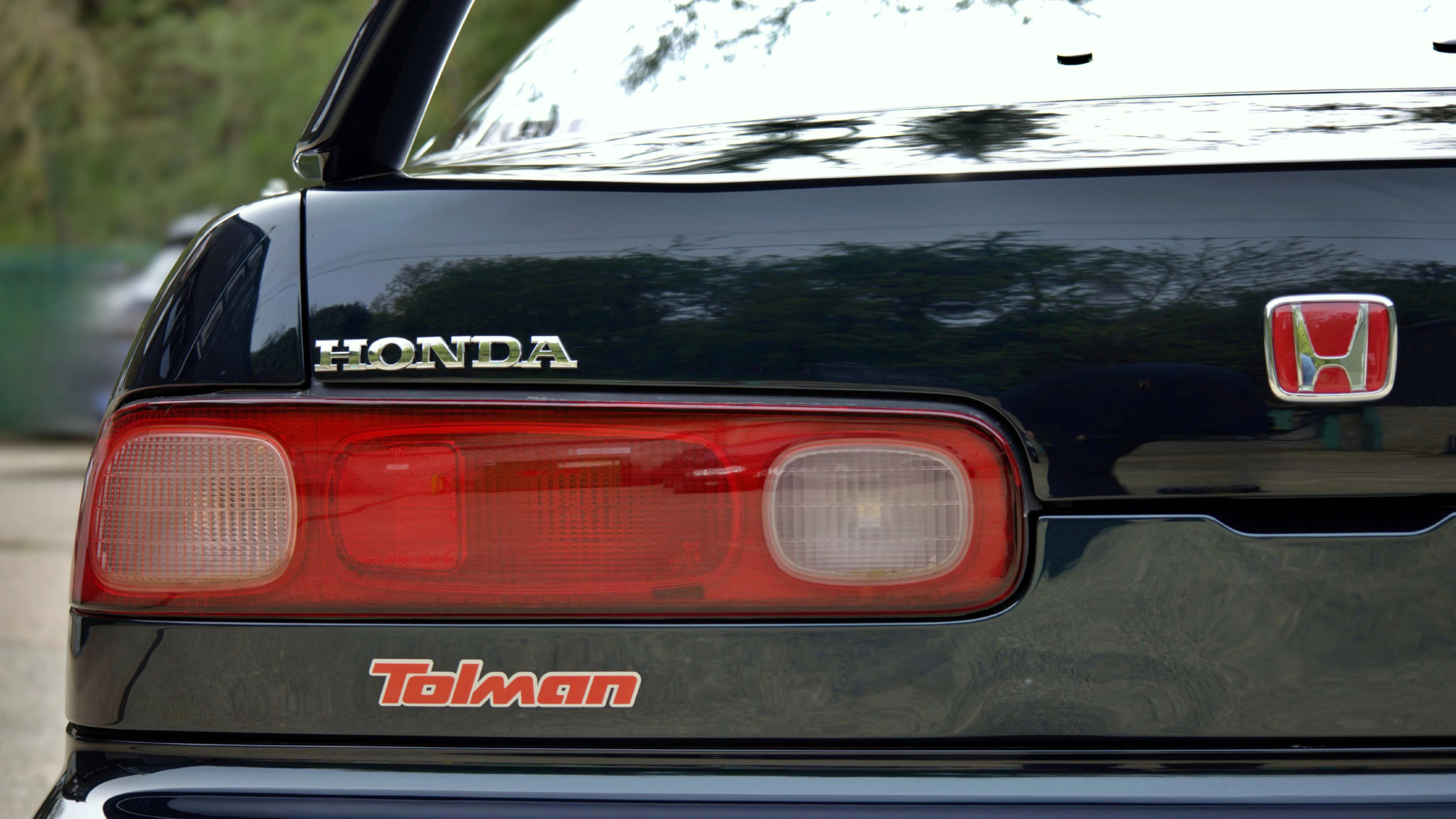 Rear end of a black Honda car with red and white taillights and a red "Tolman" badge.