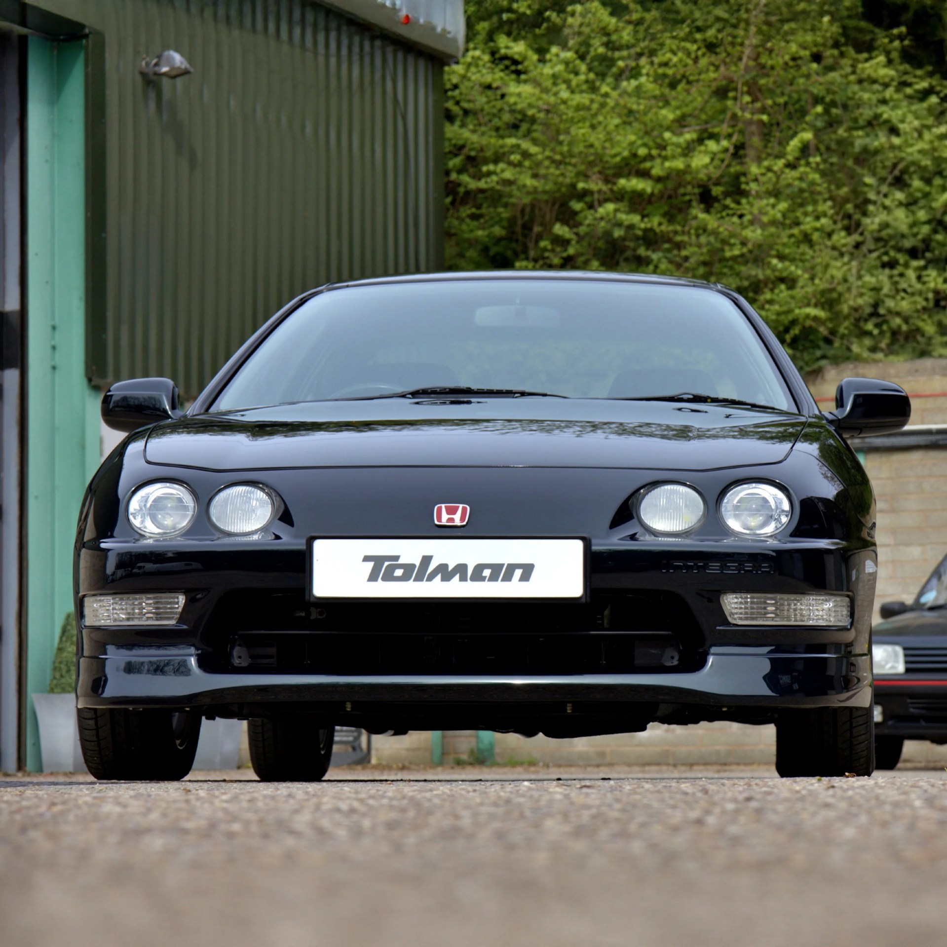 Front view of a black Honda Integra with Tolman license plate parked on a gravel surface.