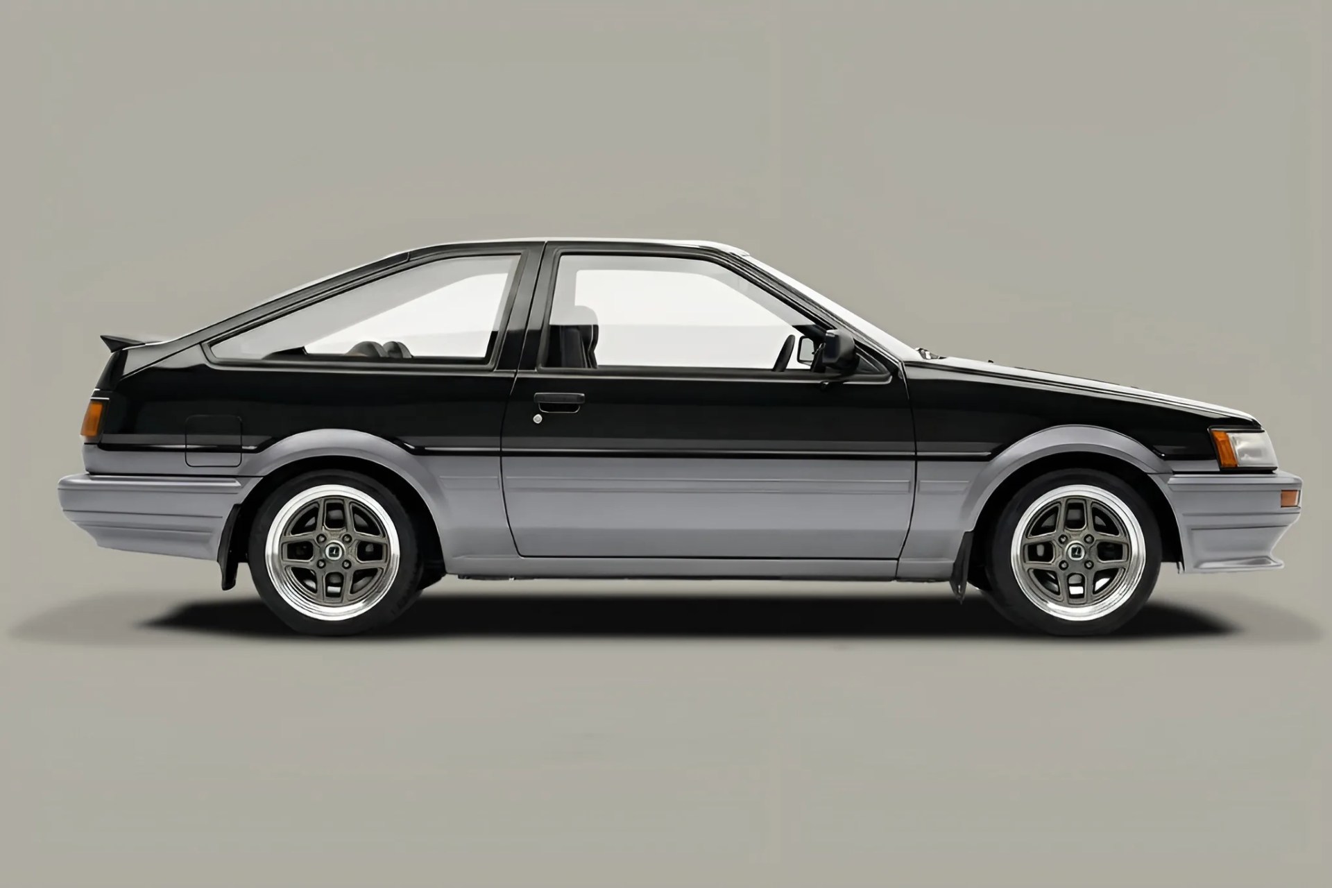 Two-tone black and gray vintage hatchback car with sporty alloy wheels on a plain background.