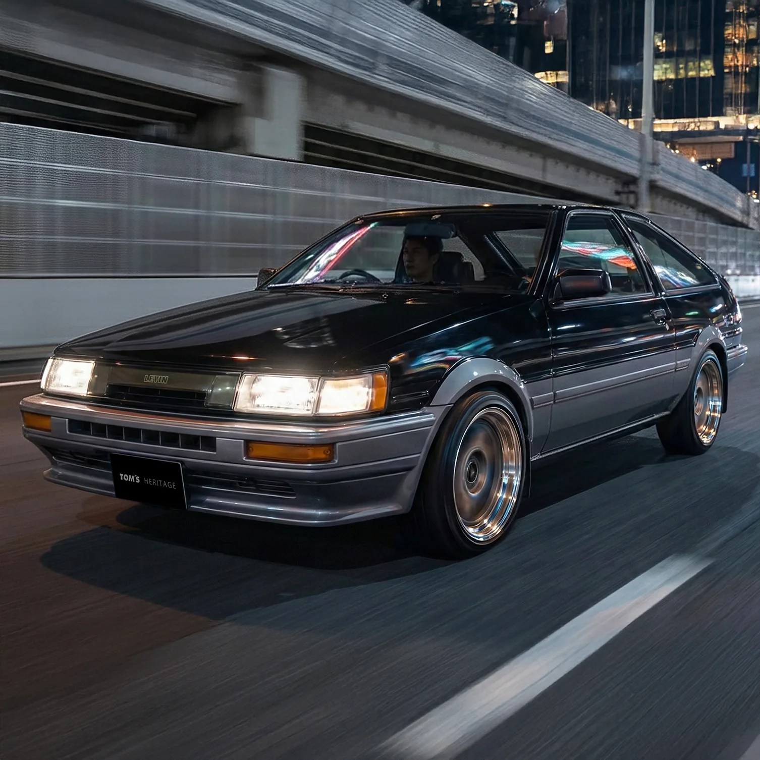 Black and gray vintage Toyota Levin hatchback driving on a city street at night.