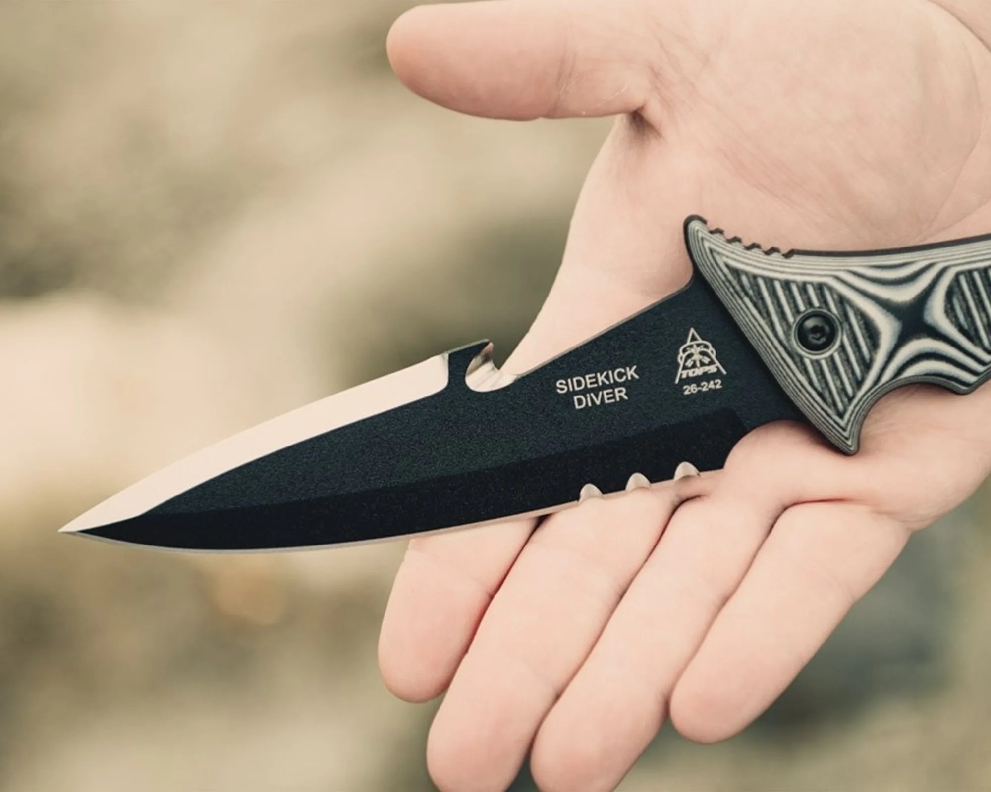 Hand holding a black fixed-blade knife with textured handle and "SIDEKICK DIVER" text on the blade.