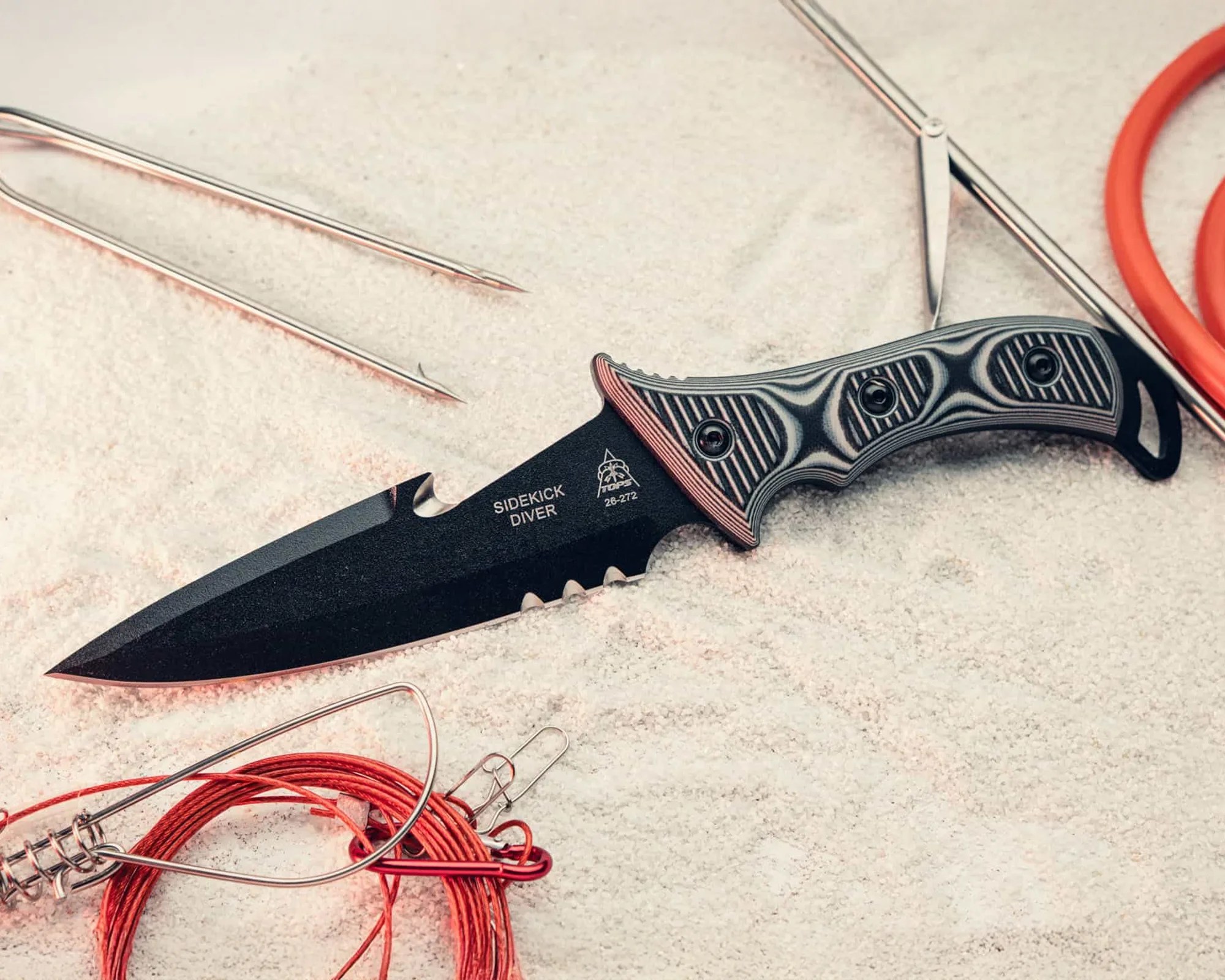 Black Sidekick Diver knife with textured handle and red fishing line on sand.