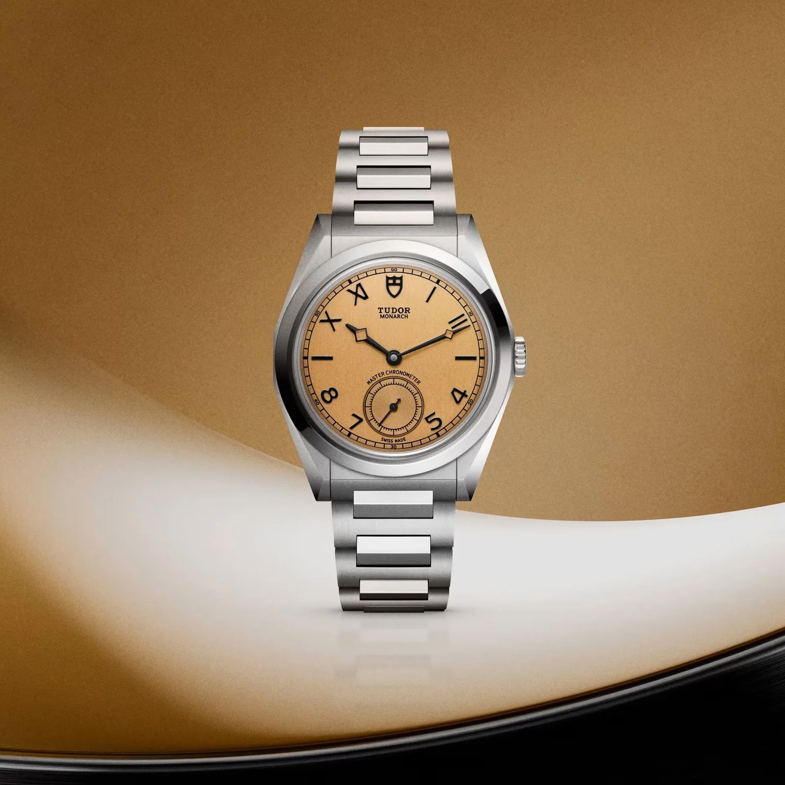 Stainless steel Tudor Monarch wristwatch with a beige dial and black Roman and Arabic numerals.