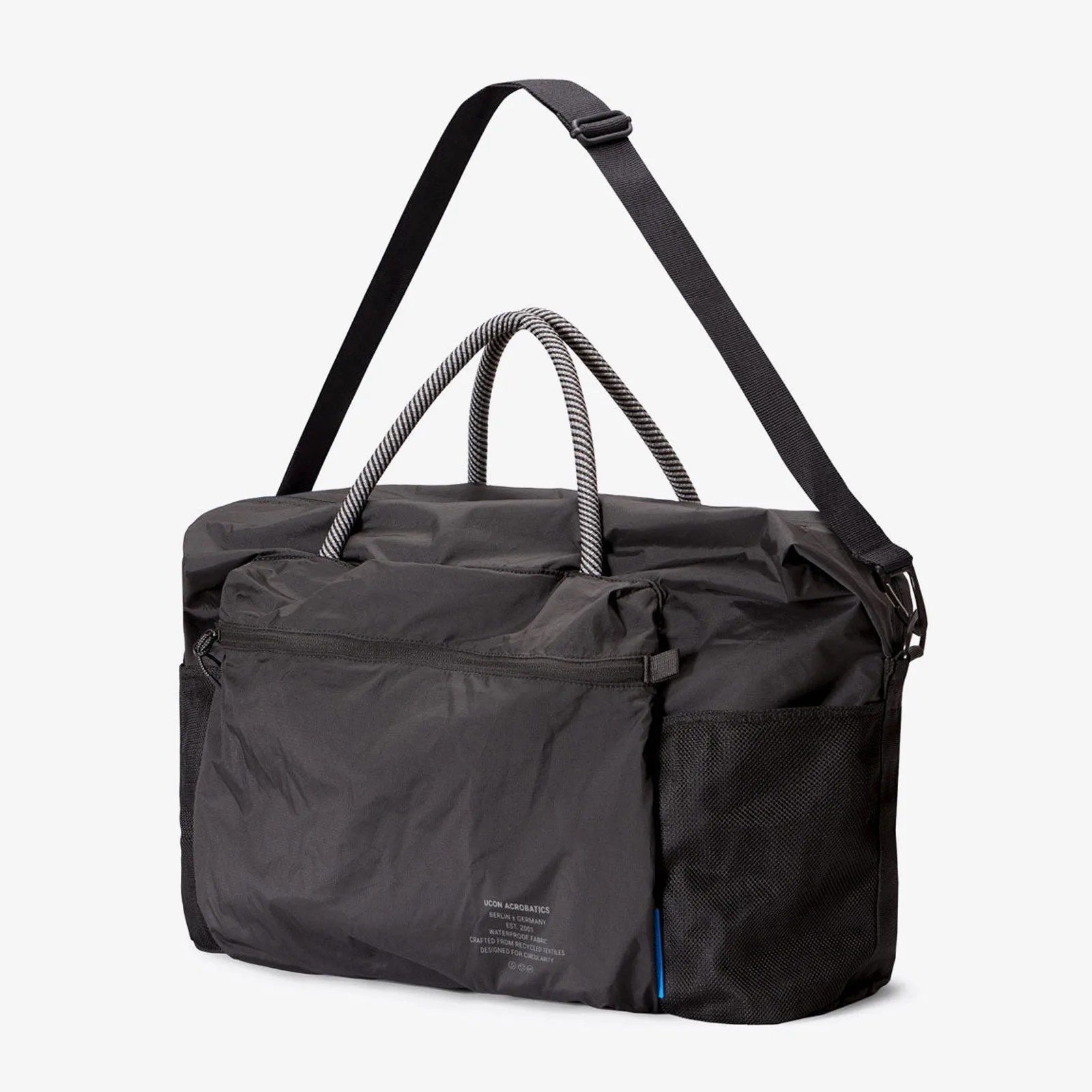 Black duffel bag with striped rope handles, adjustable shoulder strap, front zip pocket, and mesh side pocket.