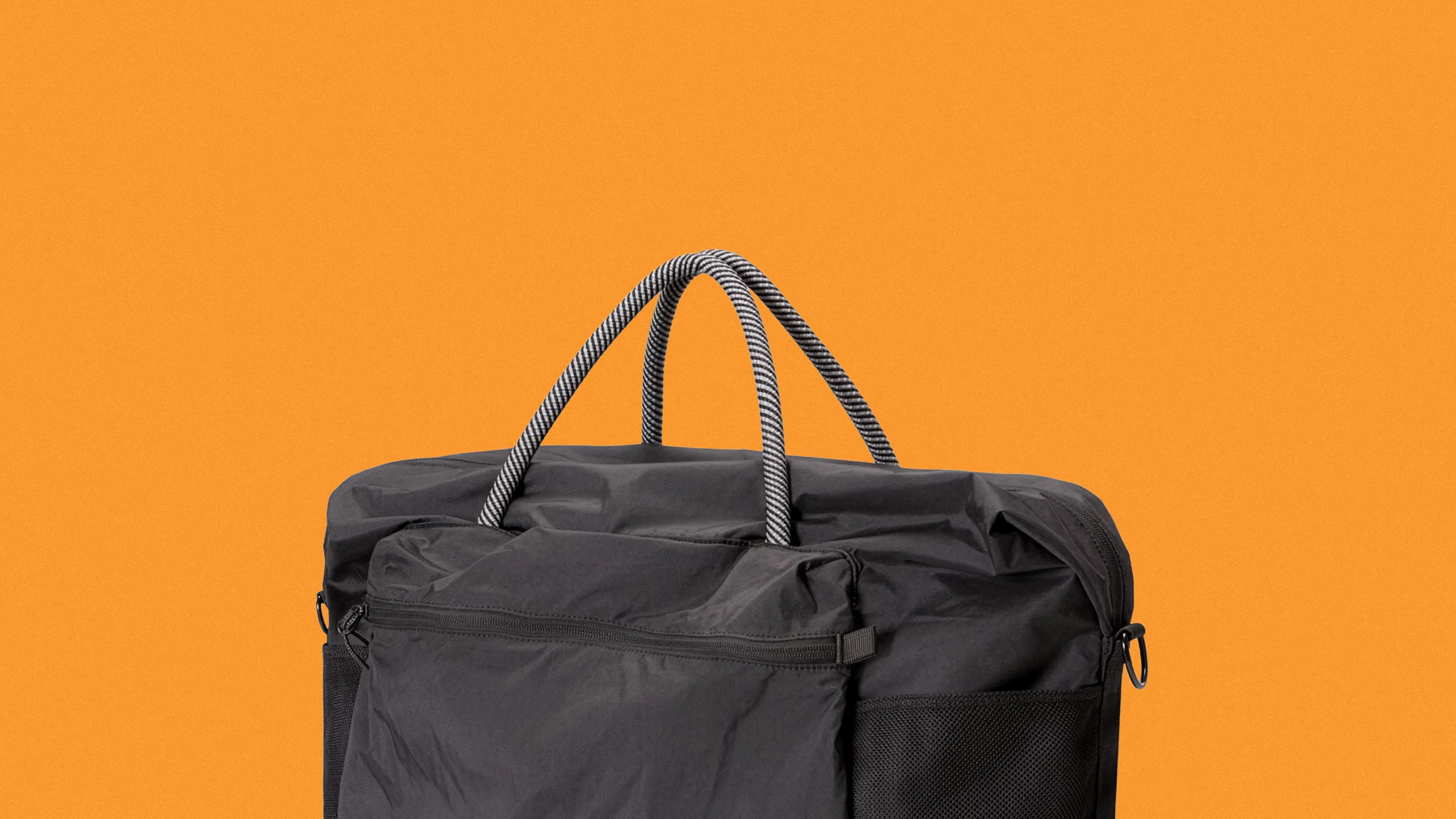 Black fabric bag with striped rope handles against an orange background.