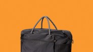 Black fabric bag with striped rope handles against an orange background.