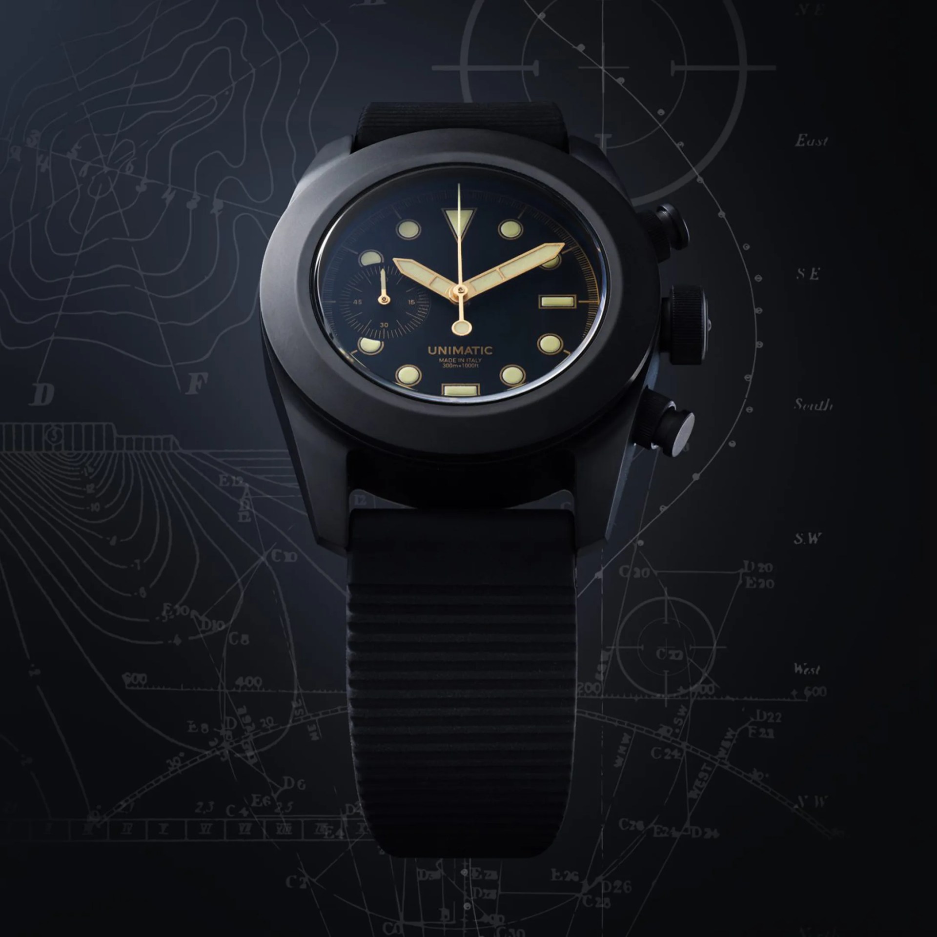 Black Unimatic wristwatch with gold-tone hands and markers on a black textured strap against a dark nautical chart background.