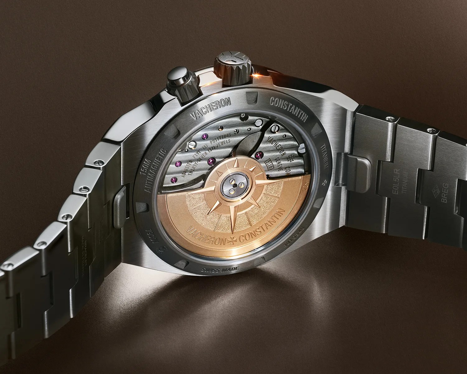 Back of a Vacheron Constantin wristwatch showing its intricate mechanical movement with a gold rotor and titanium bracelet.