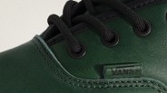 Close-up of green Vans shoe with black laces threaded through black eyelets and visible Vans logo tag.