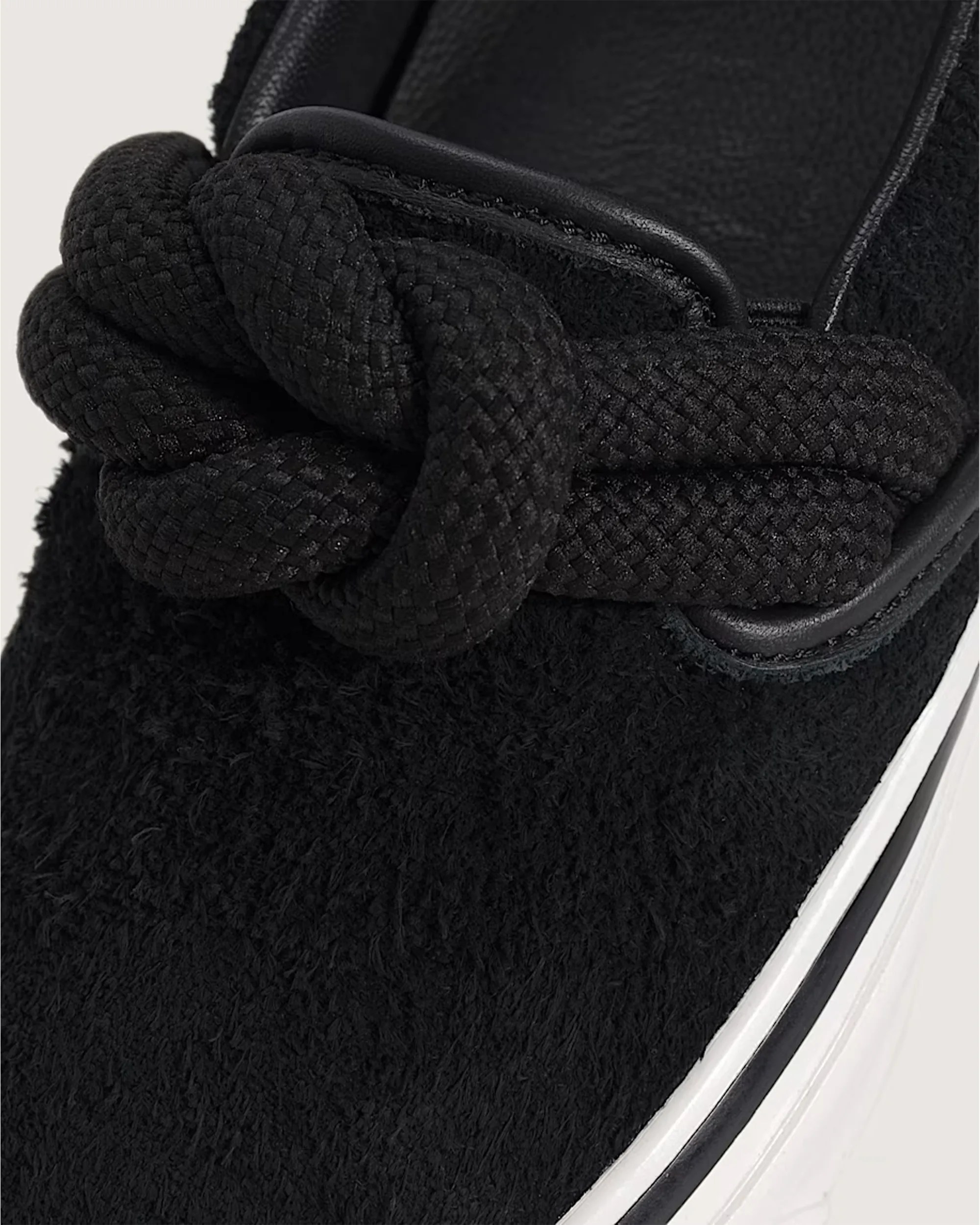 Close-up of a black textured sneaker toe with thick braided black laces and a white sole edge.