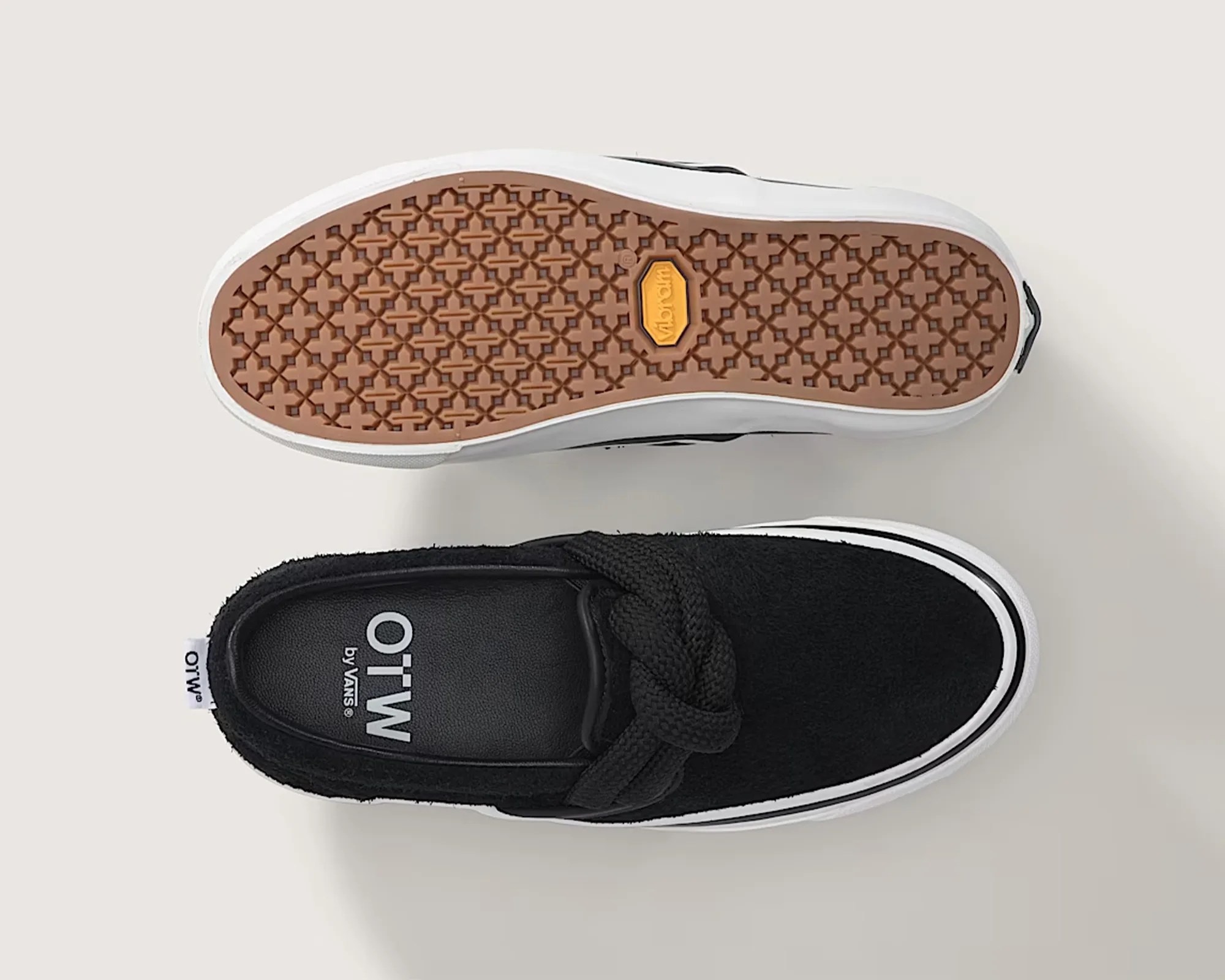 Pair of black slip-on sneakers with thick braided laces, white midsoles, and brown patterned rubber soles.
