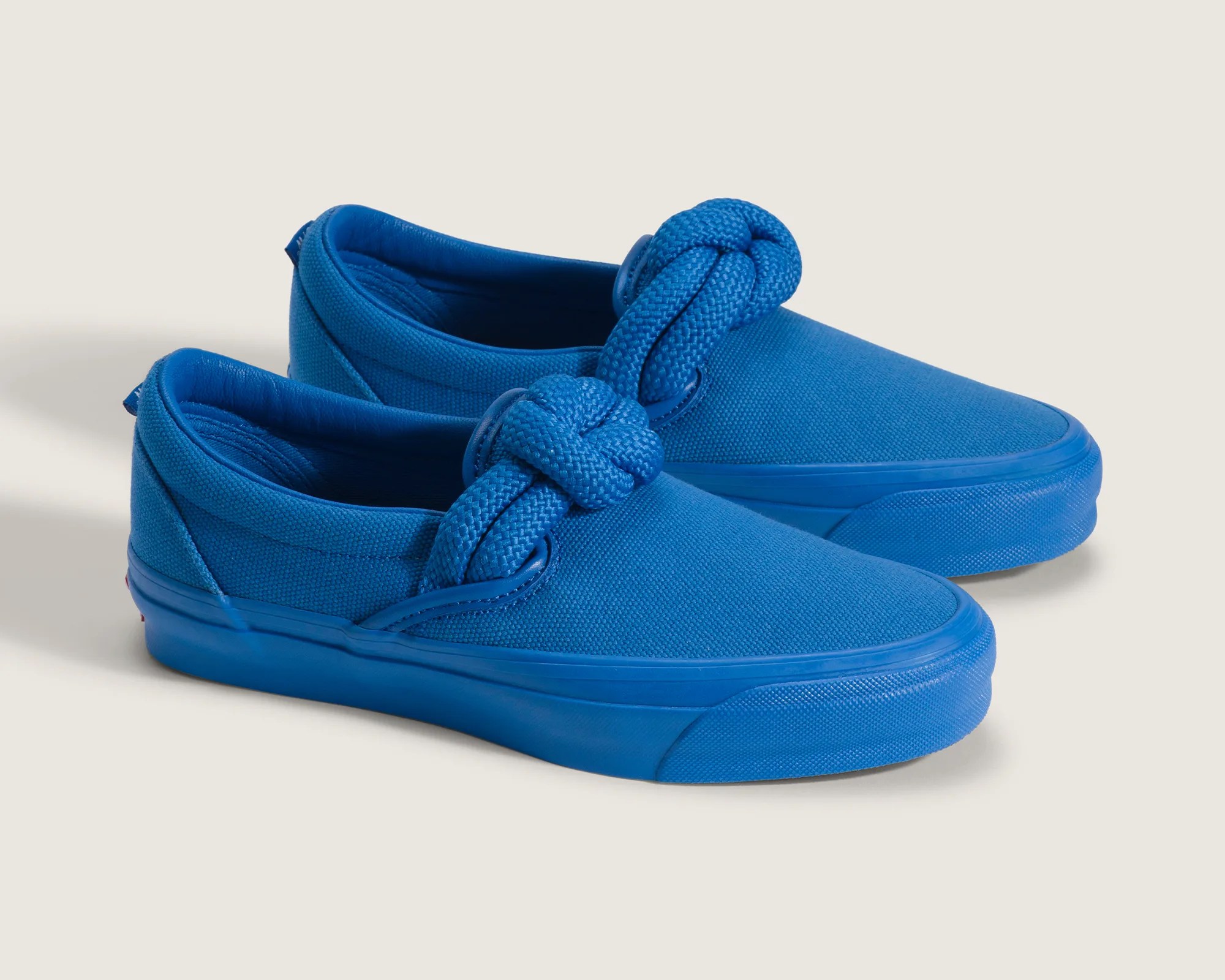 Pair of bright blue slip-on canvas sneakers with thick knotted laces and rubber soles on a light background.