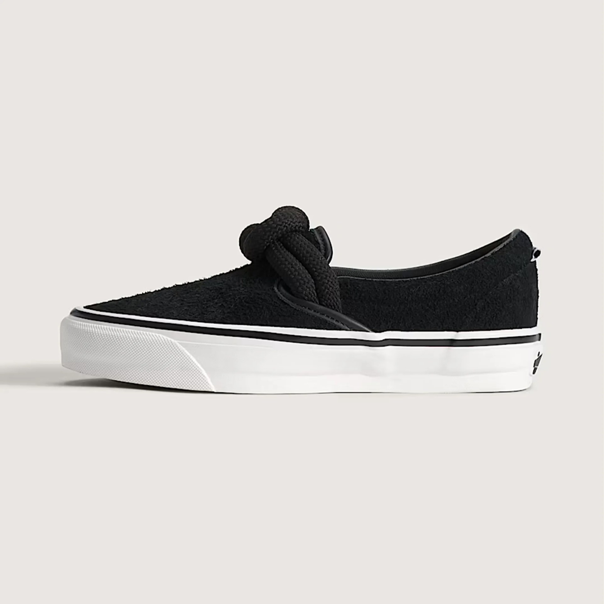 Black textured slip-on sneaker with thick knotted laces and white rubber sole with black stripe.