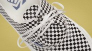 Close-up of a black and white checkered Vans sneaker with white laces on a yellow background.
