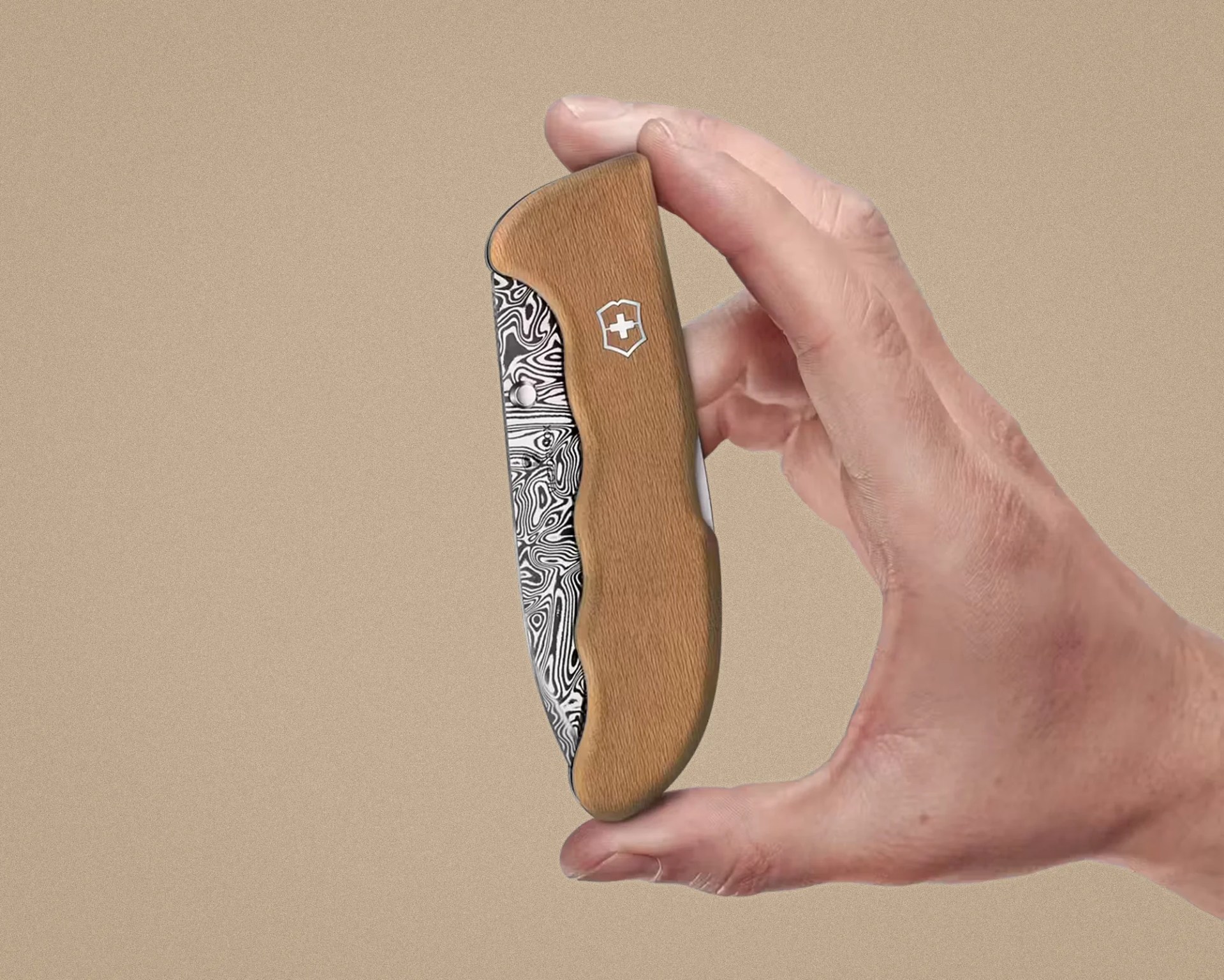 Hand holding a closed folding knife with a wooden handle and patterned metal blade.