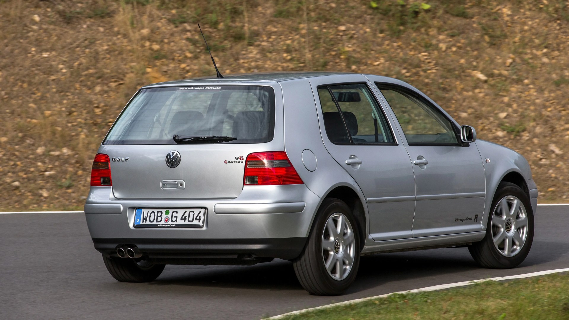 Silver Volkswagen Golf V6 4Motion hatchback driving on a paved road with a grassy and rocky background.