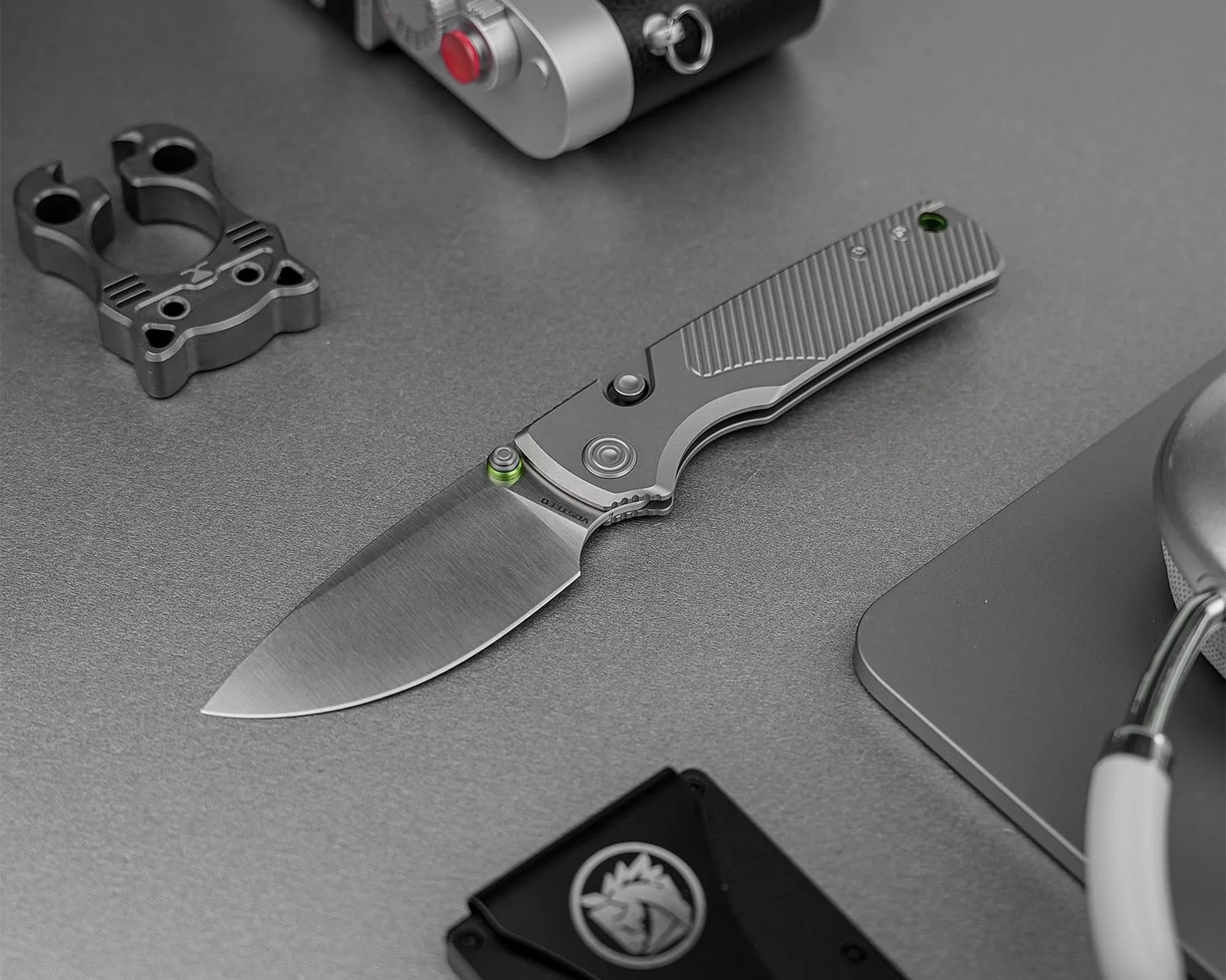 Gray folding knife with a textured handle and a wide blade on a gray surface.